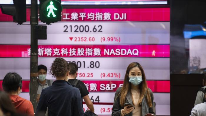 HONG KONG, CHINA - MARCH 13: Pedestrians wearing a face mask as a precautionary measure against the coronavirus, oficially named COVID-19, are seen walk past a stock market display board showing the Hang Seng Index results in Hong Kong on March 13, 2020. World markets have plunged by fears over the coronavirus outbreak. (Photo by Miguel Candela Poblacion/Anadolu Agency via Getty Images)