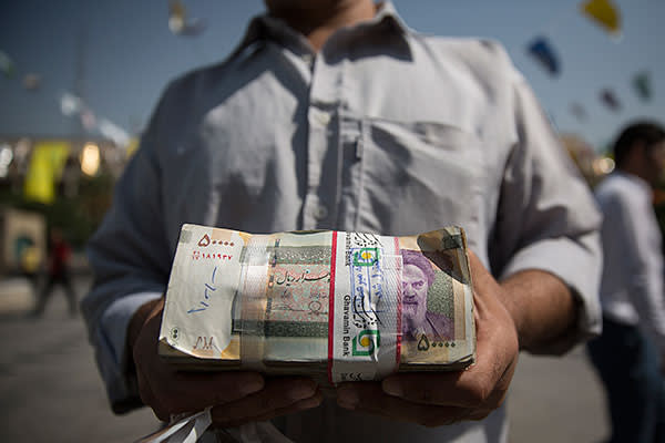 A currency trader holds a large bundle of rial banknotes outside a bazaar in this arranged photograph in Tehran, Iran, on Saturday, Aug. 22, 2015