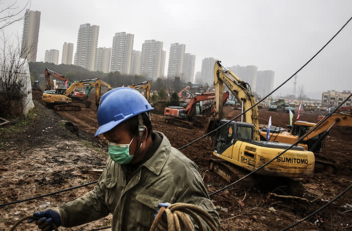 WUHAN, CHINA - JANUARY 24: (£¨ CHINA OUT£©) An electrician sets up wiring while workers drive excavators at the construction site of a field hospital on January 24, 2020 in Wuhan, Hubei Province, China. The builders will complete a 1,000-bed hospital by February 3 to cope with the surge of 2019-nCoV patients in the city. (Photo by Getty Images)