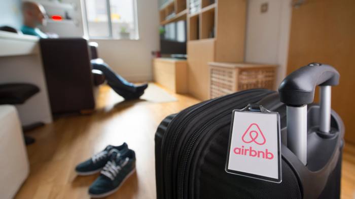 GD5G54 A man sits alone near to a suitcase with an Airbnb branded luggage tag in an otherwise empty apartment (Editorial use only).