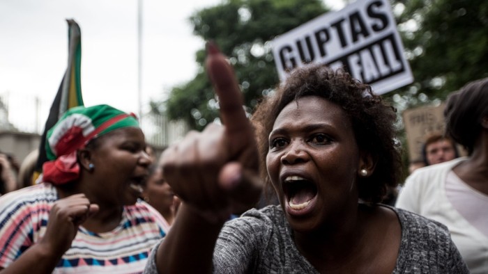 Demonstrators protesting against the South African president and calling for his resignation hold placards and shout slogans outside the Gupta Family compound in Johannesburg on April 7, 2017. Tens of thousands of protesters marched through South African cities demanding President Jacob Zuma's resignation, as a second ratings agency downgraded the country's debt to junk status. Zuma's sacking of respected finance minister Pravin Gordhan last week has fanned public anger, divisions within the ruling ANC party and a sharp decline in investor confidence in the country. Zuma has also been accused of being in the sway of the wealthy Gupta business family, allegedly granting them influence over government appointments, contracts and state-owned businesses. / AFP PHOTO / GULSHAN KHAN (Photo credit should read GULSHAN KHAN/AFP/Getty Images)