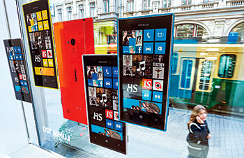 A pedestrian talks on her mobile phone as she looks at promotional material for Nokia Oyj's Windows based Lumia smartphones in the window of the company's store in Helsinki, Finland, on Tuesday, Sept. 3, 2013