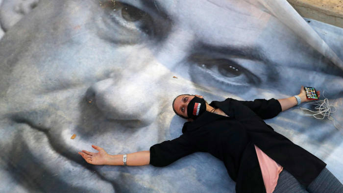 TOPSHOT - An Israeli woman wearing a face mask with " crime minister" written on it, lies on a banner during a "Black Flag" demonstration, to protest against Prime Minister Benjamin Netanyahu (image) and anti-democratic measures to contain the novel coronavirus outbreak, at Rabin Square in the coastal city of Tel Aviv, on April 19, 2020. (Photo by JACK GUEZ / AFP) (Photo by JACK GUEZ/AFP via Getty Images)