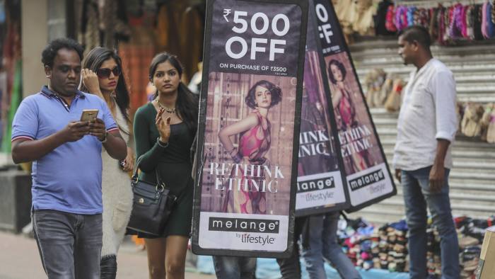 Pedestrians holding walks past people carrying advertisements for a local clothing store in Bangalore, India