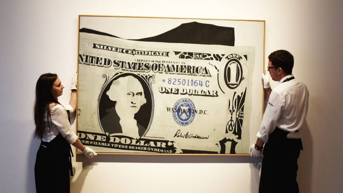 LONDON, ENGLAND - JUNE 08: Two gallery assistants pose wih 'Silver Certificate, 1962' by Andy Warhol which has an estimated value of £13-18 million and is going on show at Sotheby's on June 8, 2015 in London, England. The work is a centrepiece of an exhibition of 21 works inspired by the US Dollar which are estimated to have a total value of £50 million and will go under offer by the auction house on 1st and 2nd July 2015. (Photo by Mary Turner/Getty Images)