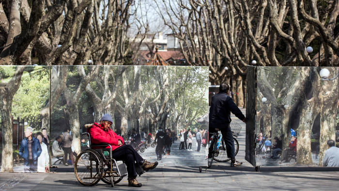 A man rests in his wheel chair in front of a park, under renovation, in downtown Shanghai on a sunny day on March 16, 2016. / AFP / JOHANNES EISELE (Photo credit should read JOHANNES EISELE/AFP/Getty Images)
