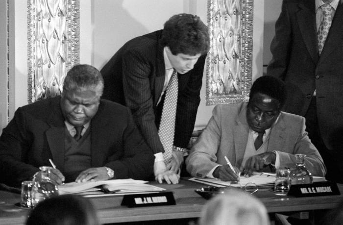 Guerrilla leaders Joshua Nkomo (L) and Robert Mugabe (R) signing the Rhodesia ceasefire agreement for the Patriotic Front at Lancaster House in London.