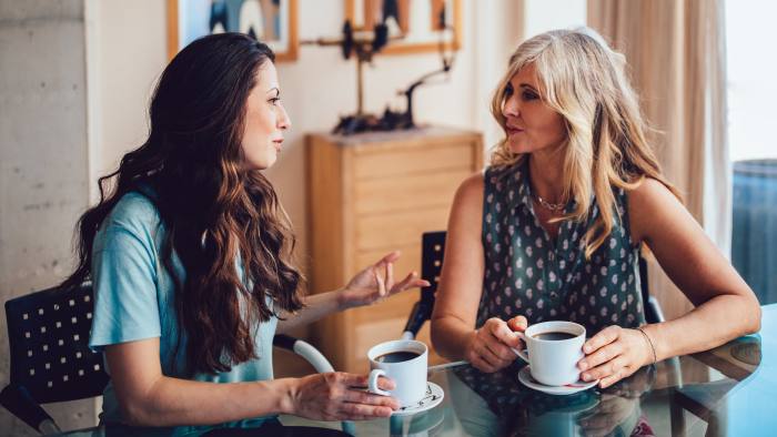 Older mother and daughter spending time together at home drinking coffee and discussing