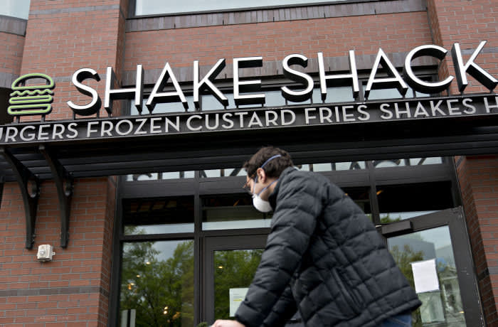 A pedestrian wearing a protective mask walks past a Shake Shack restaurant in Washington, D.C., U.S., on Monday, April 20, 2020. Shake Shack Inc. will return a $10 million loan from the U.S. government amid criticism that the publicly traded burger chain and other larger companies gobbled up the emergency funding while smaller businesses were frozen out. Photographer: Andrew Harrer/Bloomberg