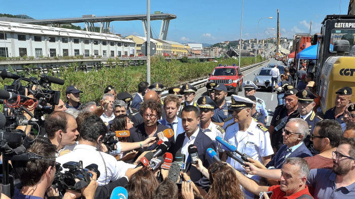 Italian Deputy Premier Luigi Di Maio, center right, and Italian Transport and Infrastructure Minister Danilo Toninelli, center left with glasses, speak to the media in front of the collapsed Morandi highway bridge in Genoa, northern Italy, Wednesday, Aug. 15, 2018. A bridge on a main highway linking Italy with France collapsed in the Italian port city of Genoa during a sudden, violent storm, sending vehicles plunging 90 meters (nearly 300 feet) into a heap of rubble below. (Alessandro Di Marco/ANSA via AP)