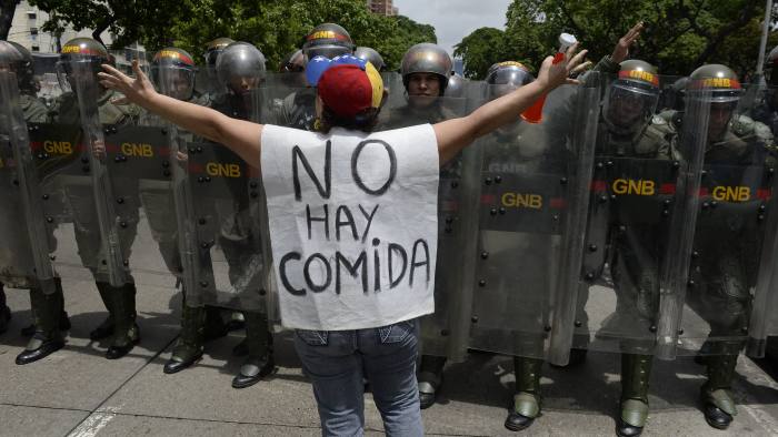 A woman with a sign reading "There is no food" protests against in front of a line of policemen in Caracas