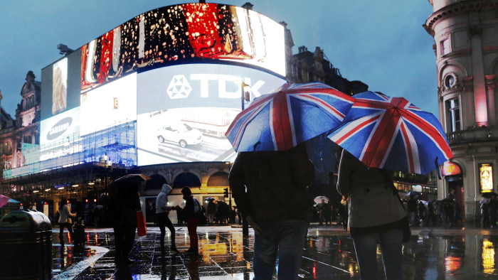 People stand under Union Flag umbrellas during rain in Piccadilly Circus in London
