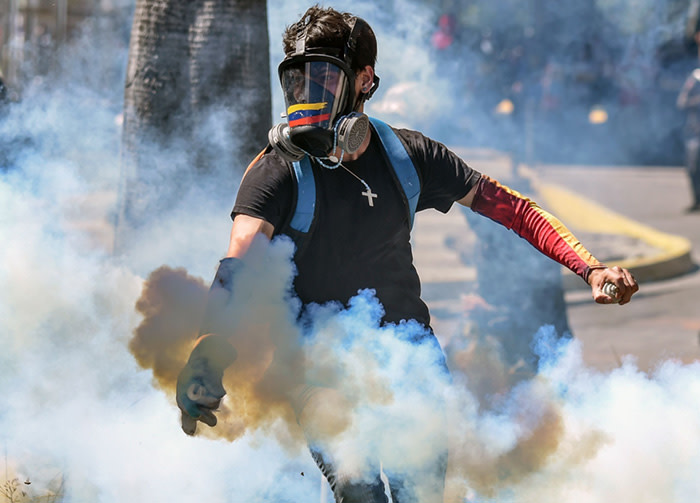 TOPSHOT - A demonstrator throws a tear gas canister back at the riot police during clashes in Caracas on January 22, 2018 which erupted during a protest to condemn the death of dissident former police officer Oscar Perez - gunned down in a bloody police operation on February 16. Perez, whose body was buried by the government on January 21 against his family's wishes, was Venezuela's most wanted man since June when he flew a stolen police helicopter over Caracas dropping grenades on the Supreme Court and opening fire on the Interior Ministry. / AFP PHOTO / Juan BARRETOJUAN BARRETO/AFP/Getty Images
