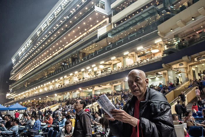 In this picture taken on March 31, 2016, spectators attend the night horse races at the Hong Kong Jockey Club in the Happy Valley district of Hong Kong. Hong Kong has two racecourses, Happy Valley and Sha Tin, with meets on Wednesday and Sundays drawing hardcore enthusiasts glued to form guides, and casual visitors more interested in a cold beer than the horses. / AFP / Anthony WALLACE / To go with AFP story: Hong Kong-racing-economy, FEATURE by Dennis Chong (Photo credit should read ANTHONY WALLACE/AFP/Getty Images)