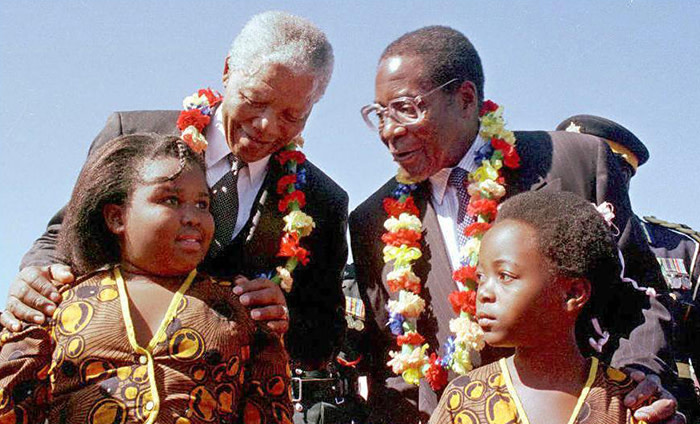 South African President Nelson Mandela (L) and Zimbabwean President Robert Mugabe are garlanded by girls after Mandela's arrival in Harare for a three-day state visit 19 May. Mandela will have two streets named in his honor and will become the first foreign head of state to address Zimbabwe's parliament. / AFP PHOTO / DAVID BRAZIER (Photo credit should read DAVID BRAZIER/AFP/Getty Images)