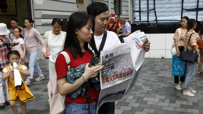 A man and a woman reads a newspaper with the headlines "Millions against Communist China shock the world" distributed in a shopping district popular with mainland Chinese tourists in Hong Kong Sunday, July 7, 2019. A march was to go through a popular shopping area for Chinese tourists and end at a high-speed rail station that connects the city to the mainland. (AP Photo/Andy Wong)