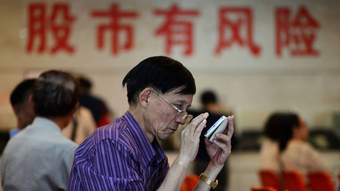 A stock investor checks his phone under Chinese writing in the background which translates as 'stock market has risk' at a brokerage house in Shanghai