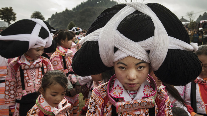 CHINA - FEBRUARY 6: Teenage girls of the Long Horn Miao ethnic minority group wear headdresses as they prepare as they gather forTiaohua or Flower Festival as part of the Lunar New Year on February 6, 2017 in Longga village, Guizhou province, southern China.The Long Horn Miao are recognized for their declining practice of wrapping a blend of linen, wool, and the hair of their ancestors around animal horns or a wooden clip to make headdresses. Many young women say they now wear the headdresses only for special occasions and festivals, as the ornaments, which are attached by the horns to their real hair, have proved impractical for modern daily life in a fast changing world. China officially recognizes 56 different ethnic minorities, and statistics show over 7 million Chinese identifying themselves as Miao. But the small Long Horn Miao community counts only around 5000 people living in 12 villages, whose age-old traditions, language, and culture are fading. It is increasingly difficult in a modernizing China, as young people are drawn from remote rural villages to opportunities in bigger cities amongst wide-scale urbanization. Farming and labour remain the mainstays of life for the Long Horn Miao, leaving the area relatively poor in comparison with many parts of China. The government has invested significant amounts into local infrastructure and the tourism industry to try to bolster the local economy. (Photo by Kevin Frayer/Getty Images)