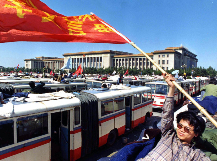 A Beijing university student waves a flag from the top of a bus parked in Tiananmen Square, Beijing, May 23, 1989, during the students strike for democracy. In the background is the Great Hall of the People. (AP Photo/Shing)