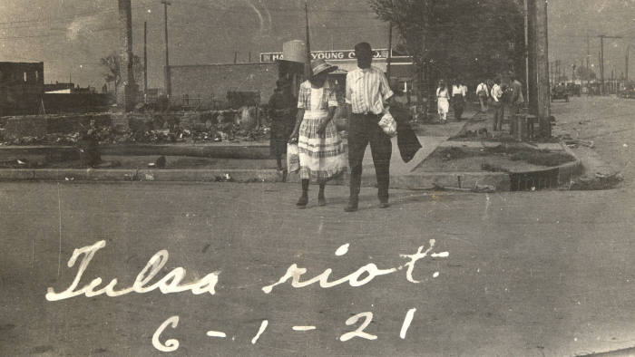 Photograph of an African American couple walking across a street with smoke rising in the distance after the Tulsa Race Riot, Tulsa, Oklahoma, June 1921. (Photo by Oklahoma Historical Society/Getty Images)