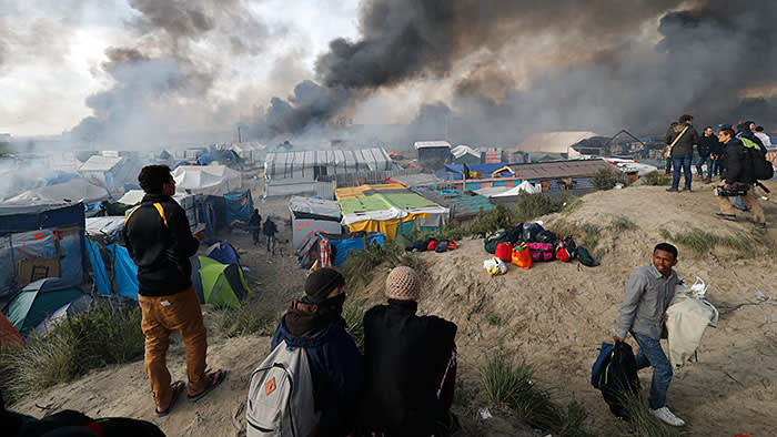 Smoke rises the sky as migrants and journalists look at burning makeshift shelters and tents in the "Jungle" on the third day of their evacuation and transfer to reception centers in France, as part of the dismantlement of the camp in Calais, France, October 26, 2016.          REUTERS/Philippe Wojazer TPX IMAGES OF THE DAY - LR1ECAQ0UA87V