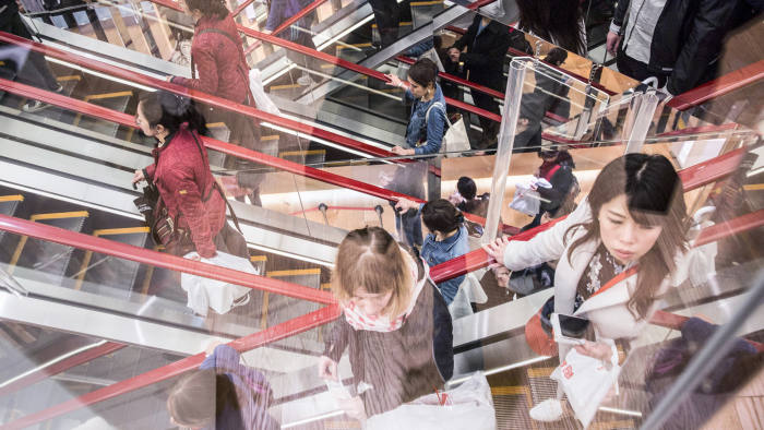 Customers ride an escalator at a Uniqlo store, operated by Fast Retailing Co., in the Ginza district of Tokyo, Japan
