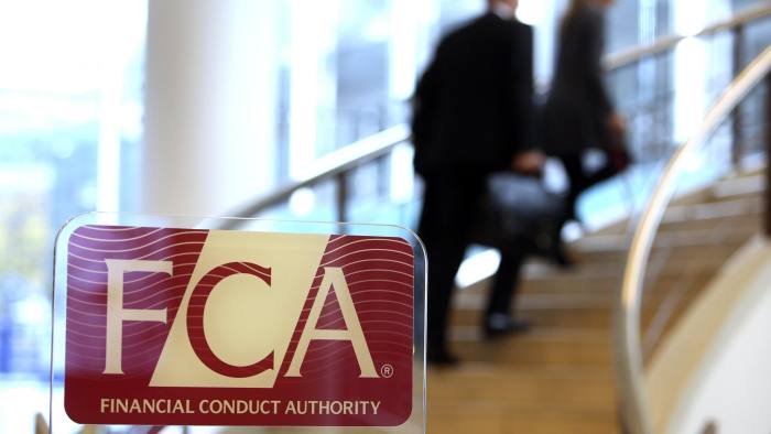 Visitors walk up a staircase as a logo sits on a sign in the reception area of the Financial Conduct Authority