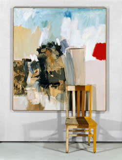 A painting in blue and white layered with paper and fabric collage, with a kitchen chair in front