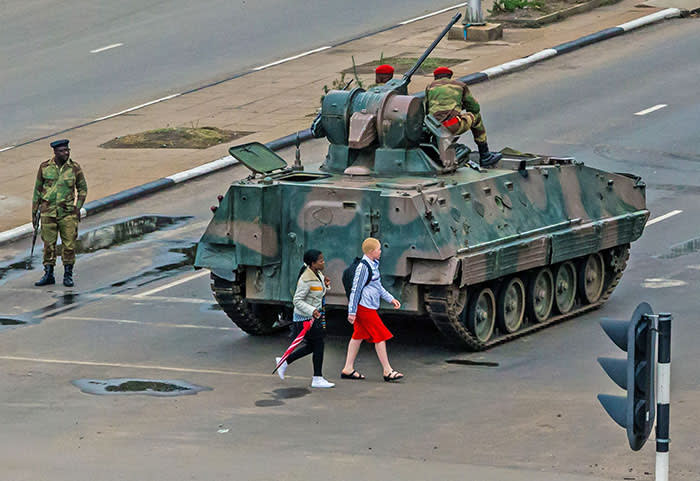 TOPSHOT - Young women walk past an armoured personnel carrier that stations by an intersection as Zimbabwean soldiers regulate traffic in Harare on November 15, 2017. Zimbabwe's military appeared to be in control of the country on November 15 as generals denied staging a coup but used state television to vow to target "criminals" close to President Mugabe. / AFP PHOTO / Jekesai NJIKIZANAJEKESAI NJIKIZANA/AFP/Getty Images