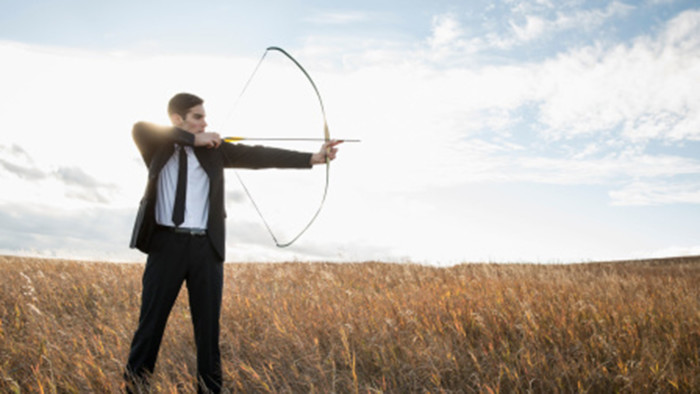Businessman taking aim with bow and arrow in field