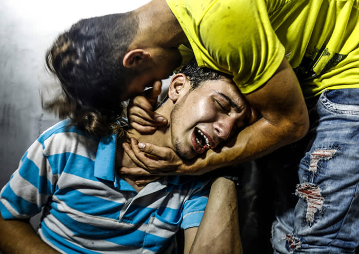 TOPSHOT - Palestinian youths mourn at al-Shifa hospital morgue on July 14, 2018 after two teenagers were killed in one of a series of Israeli raids. Aged 15 and 16, two Palestinians were on a road west of Gaza City when an air strike struck a nearby empty building, the enclave's health ministry said. Israel unleashed a wave of strikes against Gaza on July 14, while scores of rockets were fired back across the border from the territory. / AFP PHOTO / ANAS BABAANAS BABA/AFP/Getty Images