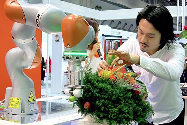 A flower arranger gets an assist by a robot in the booth of German robot manufacturer Kuka during the International Robot Exhibition at the Tokyo Big Sight on December 2, 2015 in Tokyo, Japan