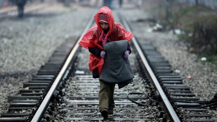 epaselect epa05187796 A boy walks on the railway line wearing a raincoat carrying a blanket at the refugee camp in Idomeni, Greece, as they wait to be allowed to cross the borders with FYROM, 29 February 2016. Macedonian police fired tear gas at hundreds of migrants after they stormed a metal fence along the border with Greece on 29 February, as refugees were blocked from travelling between the two countries on the main route to Western Europe. EPA/SIMELA PANTZARTZI
