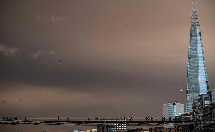 Pedestrians cross the Millennium Footbridge with the sky darkened over London on October 16, 2017 caused by warm air and dust swept up by storm Ophelia. The sun shone red and the sky darkened to a foreboding orange and brown across parts of Britain on Monday, as a storm swept air and dust in from southern Europe. Social media users shared pictures of ominous-looking clouds blocking out the sun, prompting London's Science Museum to joke on Twitter: &quot;It's not the apocalypse!&quot; Met Office forecaster Grahame Madge said the unusual effect was caused by Ophelia, the hurricane now downgraded to a violent storm which battered Ireland on Monday. / AFP PHOTO / CHRIS J RATCLIFFECHRIS J RATCLIFFE/AFP/Getty Images