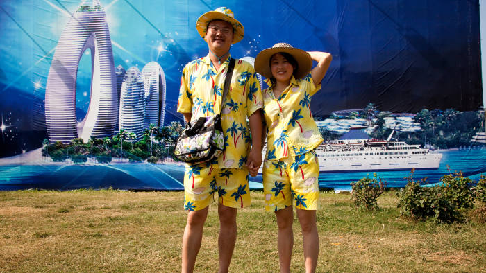 Two tourists visiting Hainan pose in front of an advert for Phoenix Island near Sanya