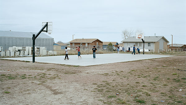 Children playing basketball and skateboarding on a court in the village of Oglala