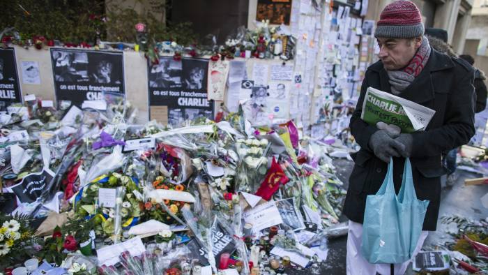 epa04559462 A man holding the new edition of the French satirical magazine Charlie Hebdo pays his respects in front of the improvised memorial on Rue Nicolas Appert, near the Charlie Hebdo headquarters, site of the 07 January attack in which 12 of the newspaper's staff were killed by two gunmen, in Paris, France, 14 January 2015. Charlie Hebdo, attacked by gunmen on 07 January, features cartoons of the prophet Muhammad in its edition, and it is published on 14 January. It will have a print run of three million, media reports said, up from an earlier announced run of one million; and far in excess of the weekly magazine's usual circulation of 60,000. EPA/IAN LANGSDON