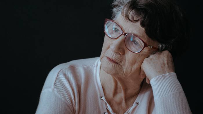 Sad senior woman with glasses sitting alone against black background