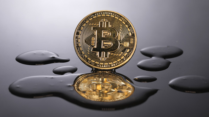A coin representing Bitcoin cryptocurrency is reflected on a polished surface as it sits in a pool of translucent liquid in the U.K. Photographer: Luke MacGregor/Bloomberg