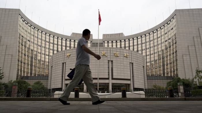 A commuter walks past the People's Bank Of China (PBOC) headquarters in the financial district of Beijing, China, on Friday, Sept. 12, 2014. Chinese Premier Li Keqiang’s options have narrowed: stimulate or miss his 2014 growth target. The weakest industrial-output expansion since the global financial crisis, and moderating investment and retail sales growth shown in data released Sept. 13, underscore the risks of a deepening economic slowdown led by a slumping property market. Photographer: Brent Lewin/Bloomberg