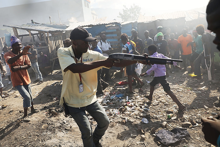 PORT-AU-PRINCE, HAITI - FEBRUARY 13: A member of a security force chases crowds with a gun following a fire at Port-au-Prince's historic Iron Market on February 13, 2018 in Port-au-Prince, Haiti. Hundreds of locals vendors lost all of their merchandise in the early morning blaze which is still under investigation. Haiti, the poorest country in the Western Hemisphere, is still reeling from President Donald Trump's comments about the Caribbean nation and his decision to revoke Temporary Protected Status (TPS) for Haitians living in America following the 2010 earthquake that claimed over 300,000 lives. Haiti is currently preparing for the start of Carnival on Sunday. (Photo by Spencer Platt/Getty Images)