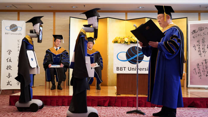 Business Breakthrough (BBT) President Kenichi Ohmae attends a graduation ceremony with Ipads attached to 'newme' robots replacing graduating students' presence, due to the coronavirus disease (COVID-19), in Tokyo, Japan March 28, 2020. BBT UNIVERSITY/Handout via REUTERS. THIS IMAGE HAS BEEN SUPPLIED BY A THIRD PARTY. NO RESALES. NO ARCHIVES - RC2YWF923N41