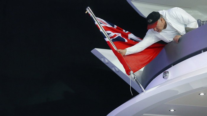 An employee places a sailing Union Jack flag on to the back of a Sunseeker International Ltd boat at the ExCel exhibition centre in preparation for the 2016 London Boat Show in London, U.K., on Thursday, Jan. 7, 2016. The event will showcase the latest luxury yachts at the London exhibition site between Jan. 8 - Jan. 17, 2016. Photographer: Chris Ratcliffe/Bloomberg