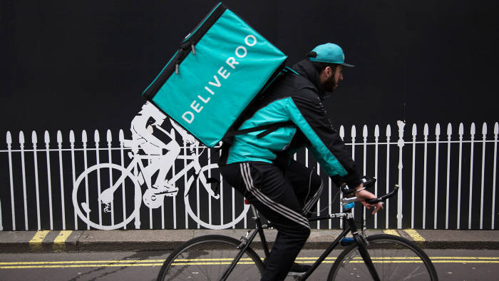 Deliveroo cycle courier with his large back box interacts with a stencilled cyclist while out delivering in London, England, United Kingdom