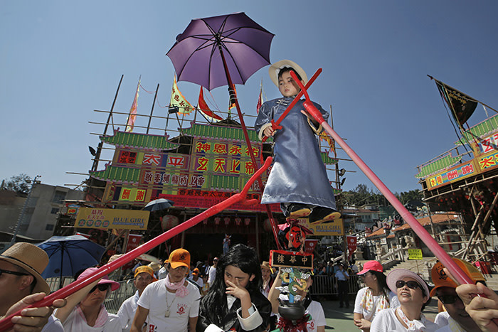 A child dressed in a traditional Chinese costume floats in the air, supported by a rig of hidden metal rods, during a parade on the outlying Cheung Chau island in Hong Kong to celebrate the Bun Festival Tuesday, May 22, 2018. Thousands of local residents and tourists flocked to an outlying island in Hong Kong to celebrate a local bun festival on Tuesday despite the recording-breaking heat. The festival features a parade with children dressed as deities floated on poles. Later on Tuesday, contestants will take part in bun-scrambling competition. They will race up a 14-meter bamboo tower to snatch as many plastics buns as possible. Buns that are higher up are worth more points. (AP Photo/Kin Cheung)