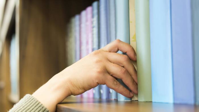 A hand taking a book from a bookshelf