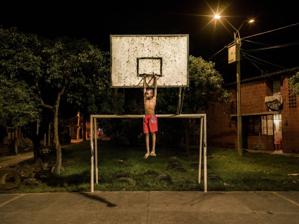 A young boy hanging from a basketball hoop.