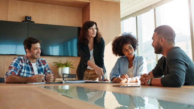 Young businesswoman discussing something with her coworkers while standing at the conference table. Multi ethnic business team meeting in office.