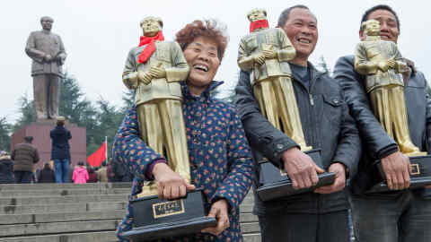 Visitors take a picture in front of the statue of Chairman Mao Zedong at the central square of his hometown Shaoshan. In their hands smaller sized statues they bought at a shop in Shaoshan.