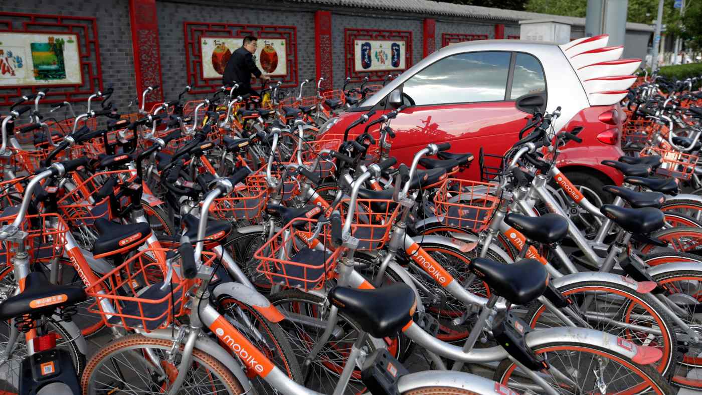 Mobike's shared bikes are parked around a car in Beijing, in April 2017.